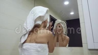 年轻女子看着镜子，沐浴后摸着脸。
